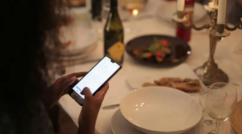 Una persona interactuando con un dispositivo móvil sobre una mesa de comedor formal, representando la paradoja de la productividad laboral y la gestión del tiempo.