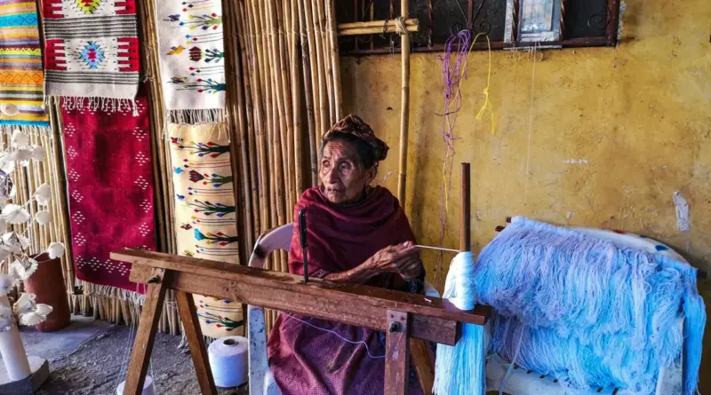 Una maestra artesana mexicana sentada en su taller frente a un telar de madera, rodeada de hilos y textiles tradicionales en blanco y negro, representando la preservación del patrimonio cultural y la auditoría de cadenas de suministro responsables.